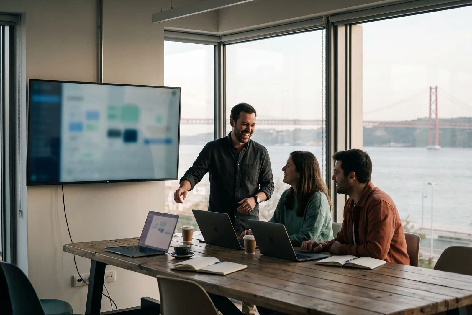A small development team talking around a shared screen in an office overlooking the Tagus