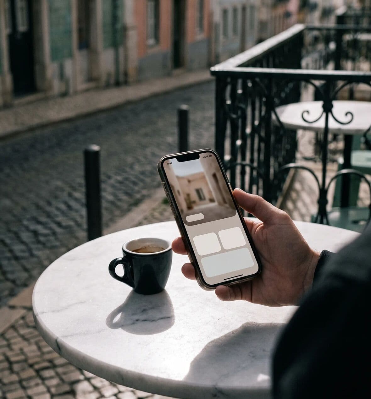 A hand holding a phone with a booking app on a sunlit Lisbon café terrace